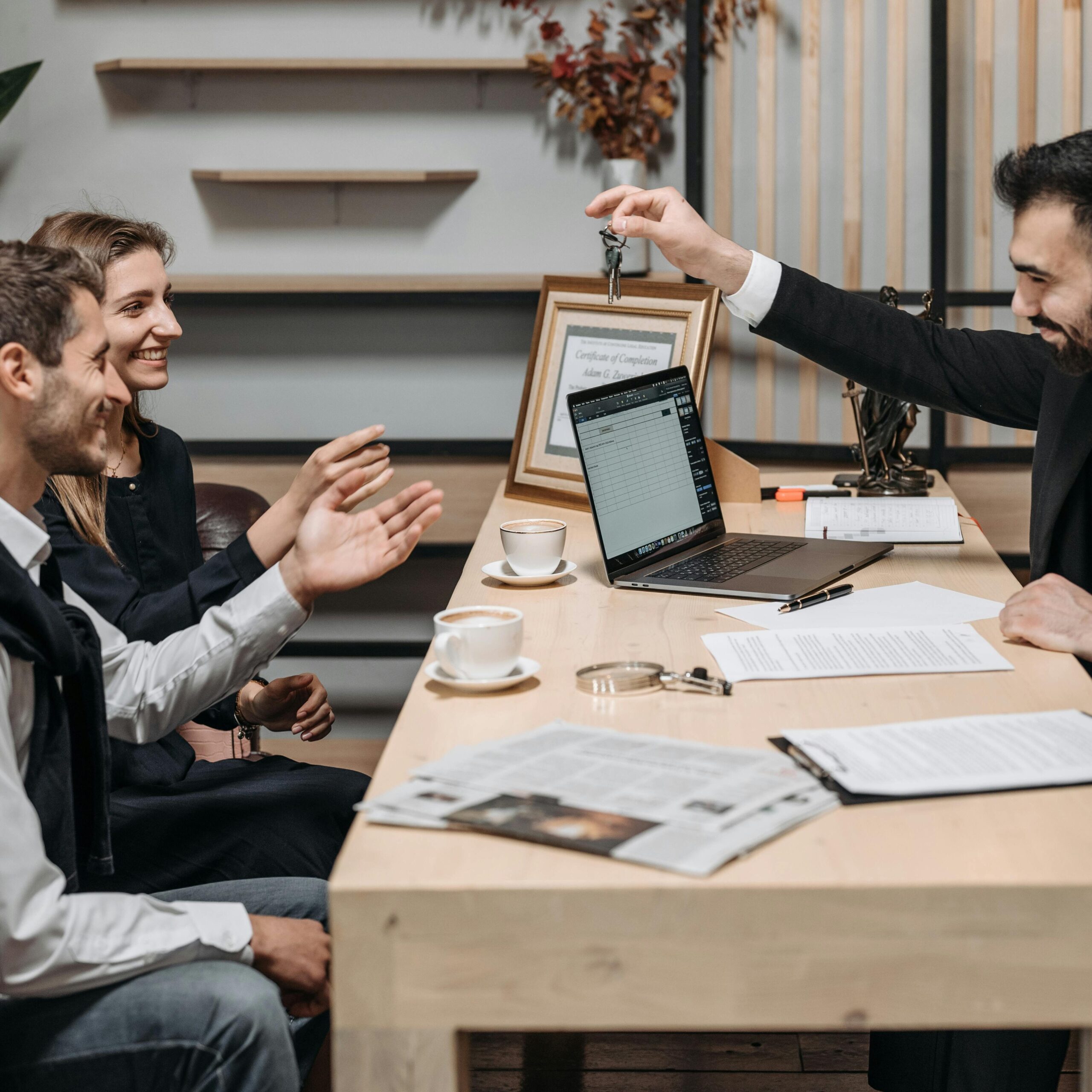 Business professional handing keys to smiling clients at an office desk during a consultation.